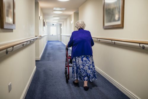 A senior woman walking down a corridor with the assistance of a walker.